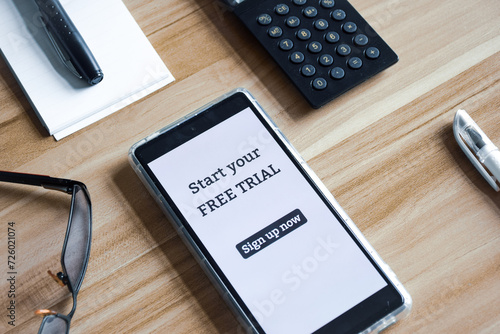 Mobile phone displaying message start your free trial sign up now. Wooden background, workplace.