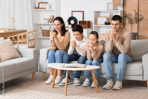 Family praying together on sofa at home photo