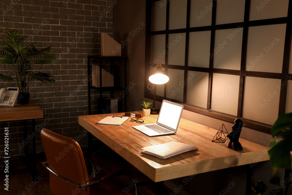 Interior of dark office with workplace and glowing lamp at night Interior of dark office with workplace and glowing lamp at night