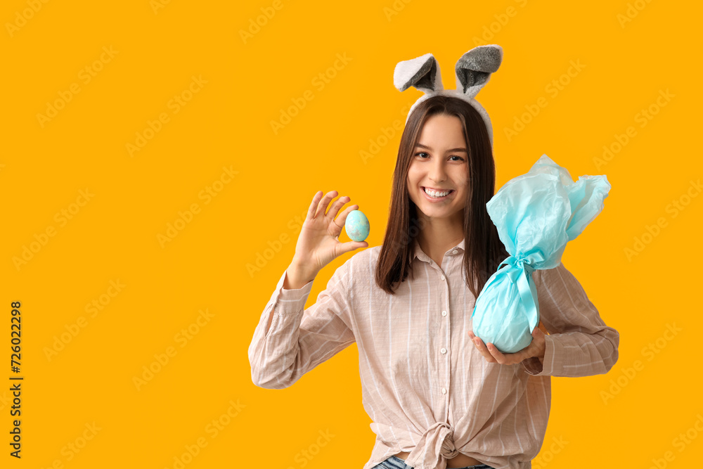 Pretty young woman with bunny ears, gift and Easter egg on yellow background Pretty young woman with bunny ears, gift and Easter egg on yellow background