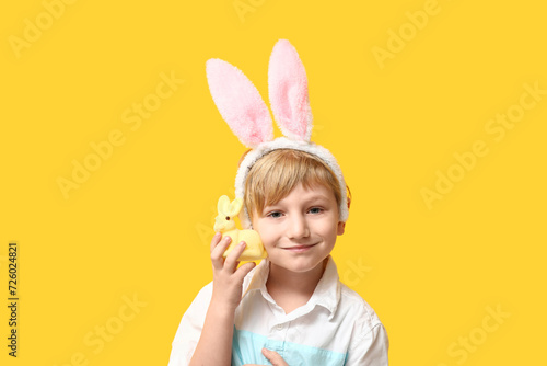 Cute little boy in bunny ears with Easter rabbit on yellow background