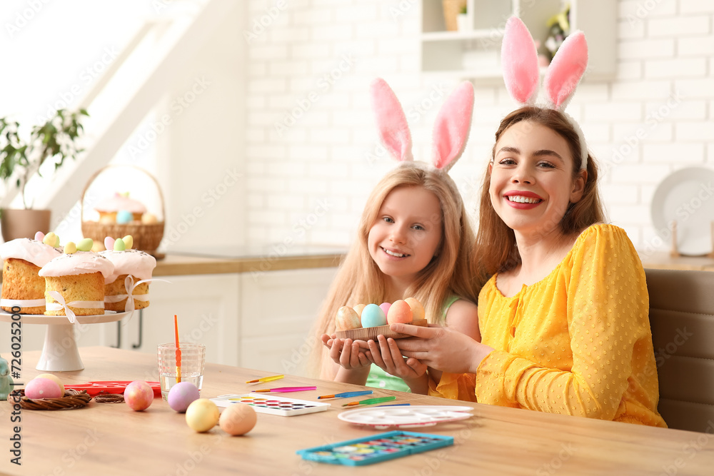 Cute little girl and her mother in bunny ears with painted Easter eggs in kitchen Cute little girl and her mother in bunny ears with painted Easter eggs in kitchen