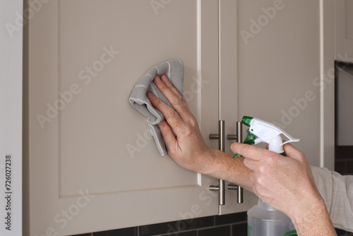 Konstfotografi Woman cleaning kitchen cabinets with a rag and spray bottle