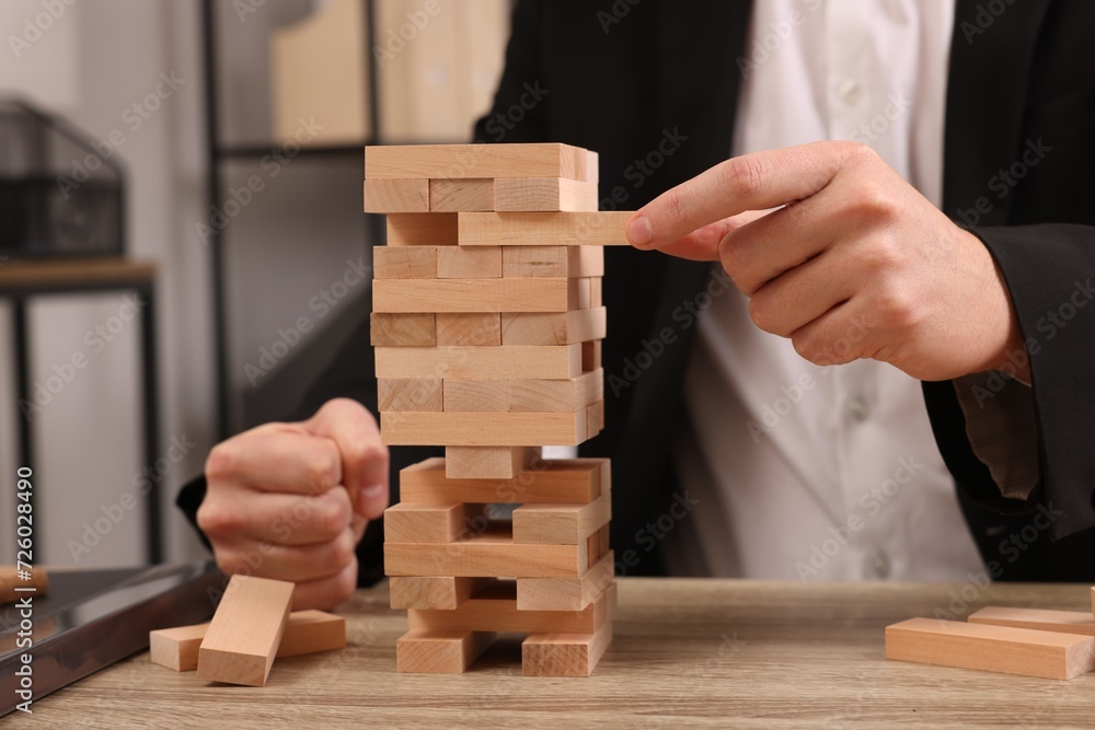 Playing Jenga. Man removing wooden block from tower at table indoors, closeup