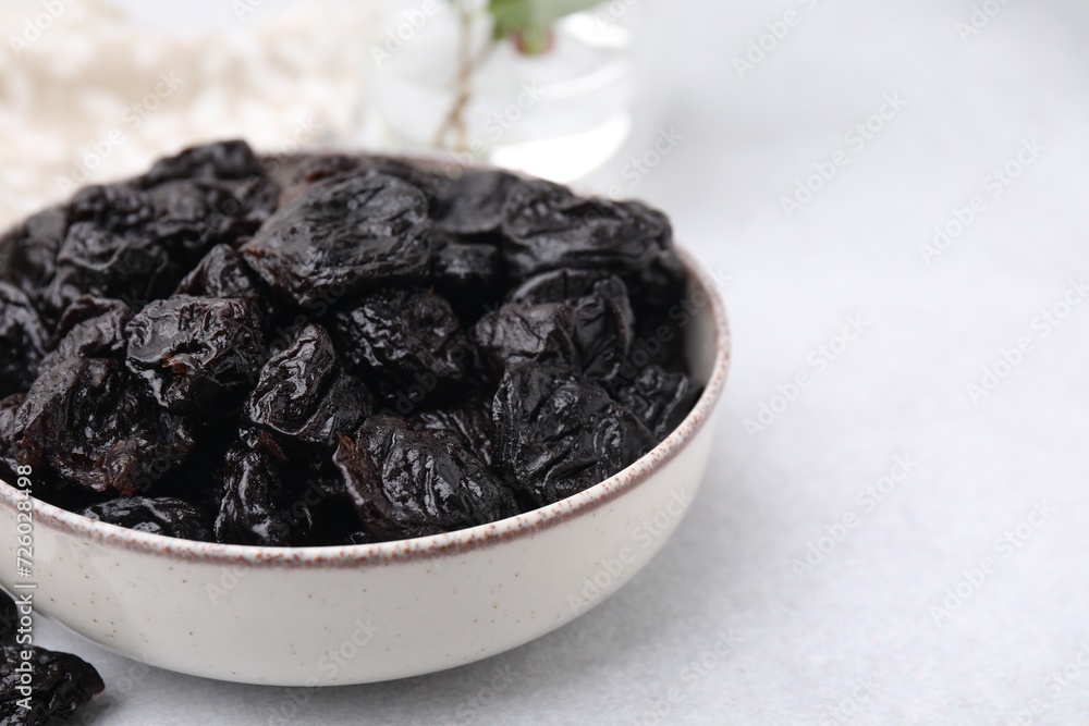 Sweet dried prunes in bowl on light table, closeup. Space for text Sweet dried prunes in bowl on light table, closeup. Space for text