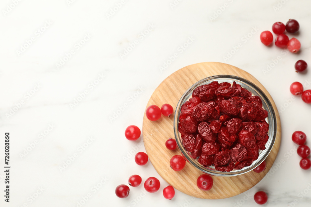 Tasty dried cranberries in bowl and fresh ones on white table, top view. Space for text