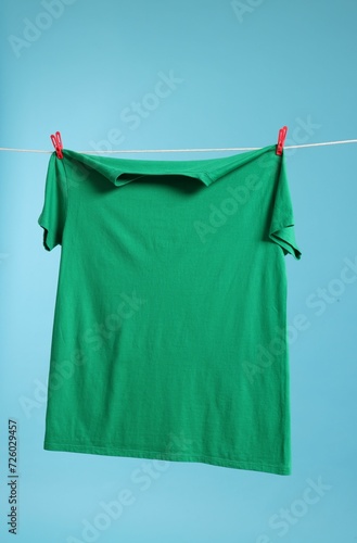 One green t-shirt drying on washing line against light blue background