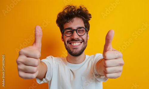 young happy man making thumbs up gesture on yellow background