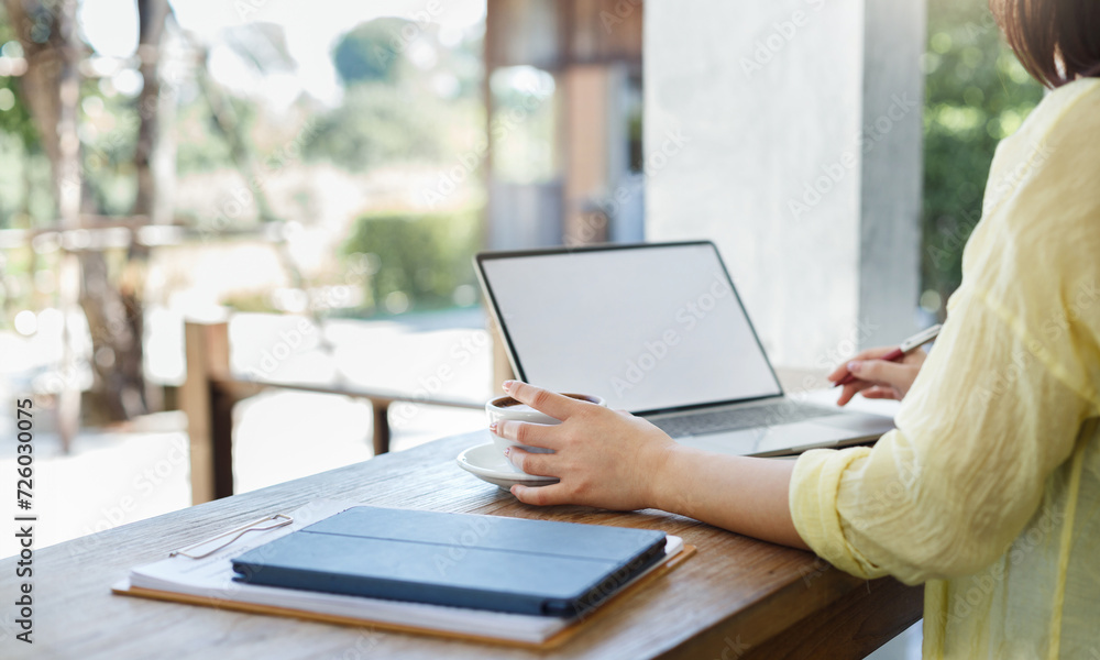 Close-up shot, young asian woman in casual clothes holding coffee cup while working with laptop at outdoor cafe Close-up shot, young asian woman in casual clothes holding coffee cup while working with laptop at outdoor cafe