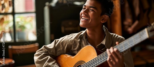 Confident Hispanic young man at a music studio, playing a classical guitar with a smile on his face, looking away with a natural, laughing expression.