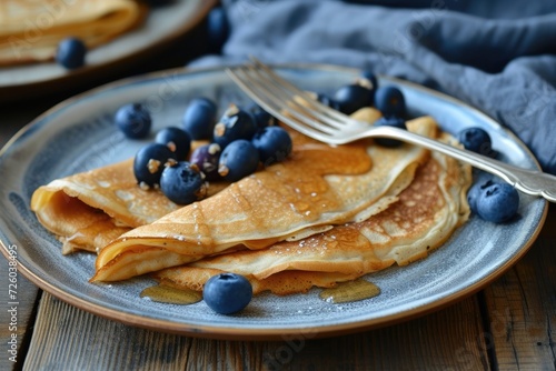 Pancake or crepe dish filled with dulce de leche accompanied by a fork and spiked blueberries