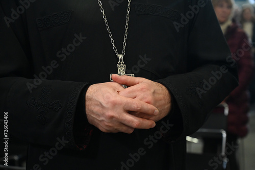 Catholic priest in liturgical vestments praying with hands folded in cathedral. Christian priest with a cross on his neck.