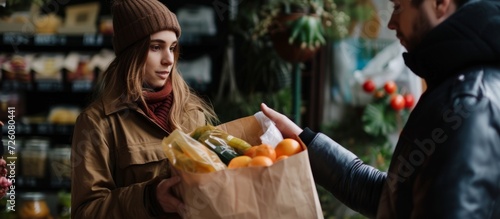 A woman receives a paper bag with food items from a man.