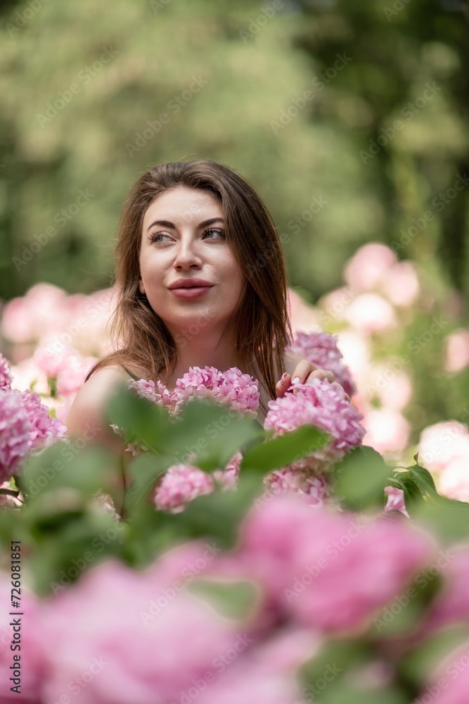 Hydrangeas Happy woman in pink dress amid hydrangeas. Large pink hydrangea caps surround woman. Sunny outdoor setting. Showcasing happy woman amid hydrangea bloom. Hydrangeas Happy woman in pink dress amid hydrangeas. Large pink hydrangea caps surround woman. Sunny outdoor setting. Showcasing happy woman amid hydrangea bloom.