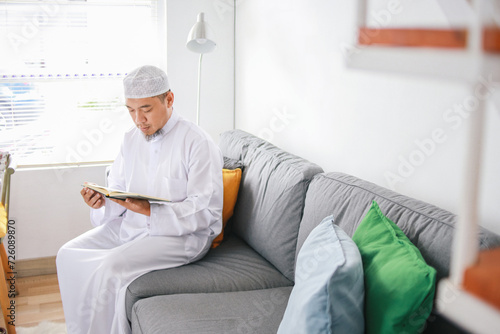 Asian muslim man sitting on sofa chair and reading the holy Quran