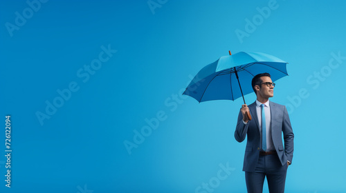 a businessman holding an umbrella against a calming blue backdrop, symbolizing protection and security provided by insurance. Generative AI. © TeacherPhoto