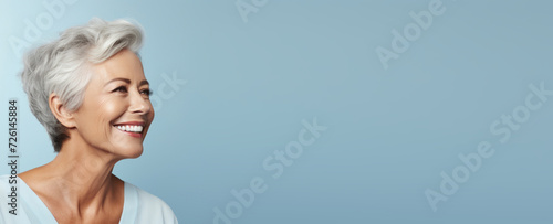 Happy mature woman with white hair laughing against a blue background.