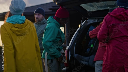 Group of diverse hikers unpack luggage and backpacks from trunk of car, settle into rented house in mountains. Tourist family or friends during vacation trip. Tourism and active leisure. Slow motion.