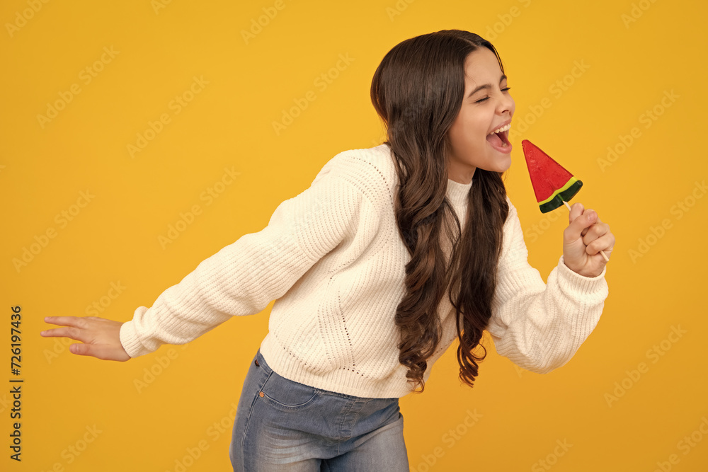 Teenager girl eating sugar lollypop. Candy and sweets for kids. Child eat lollipop popsicle over yellow isolated background. Yummy caramel, candy shop Excited teenager girl.