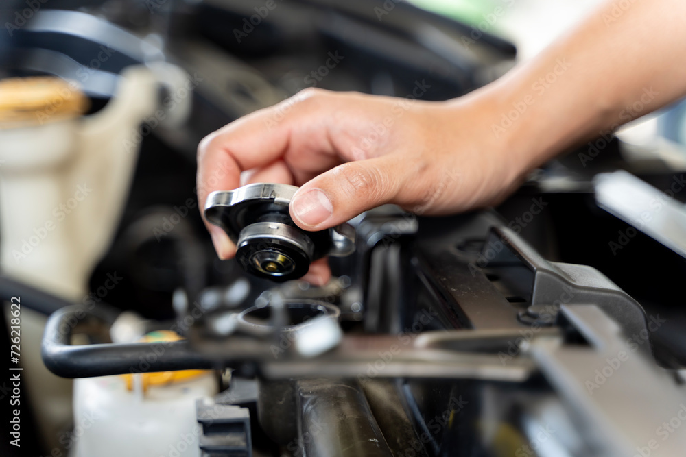 A person is holding a funnel and pouring coolant into the radiator of a car and they are standing in front of a car.