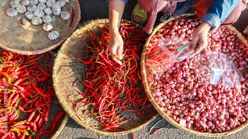 The hands of a buyer are sorting and choosing fresh chilies from rattan trays then put into plastic bags at a vegetable seller at the local farmer's market on a sunny morning. photo