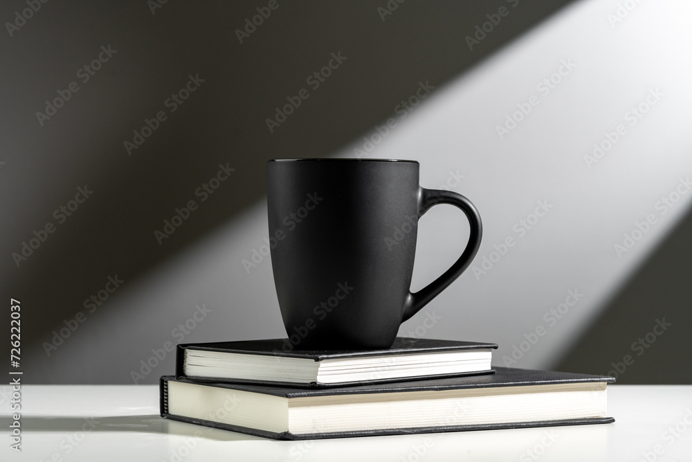 Black cup on books in sunlight on gray background Black cup on books in sunlight on gray background