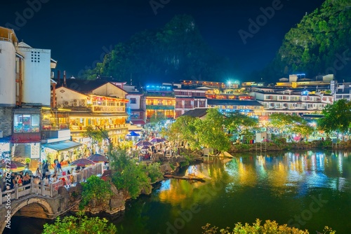 Beautiful bridge and lake in the ancient Chinese village of Yangshuo with reflections in water and the oldest and busiest West Street (Xi Jie) in the background at night. Yangshuo, Guangxi, China