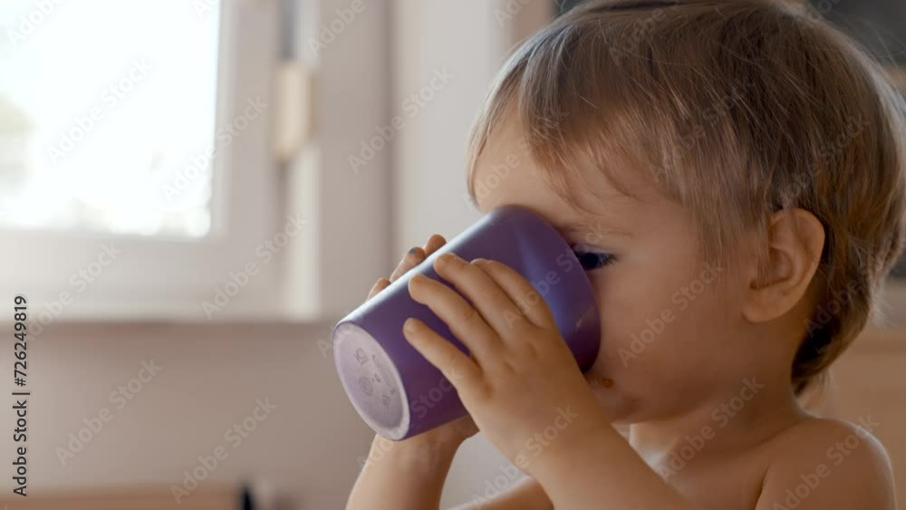 A video capturing a young child peacefully drinking from a purple cup. A video capturing a young child peacefully drinking from a purple cup.