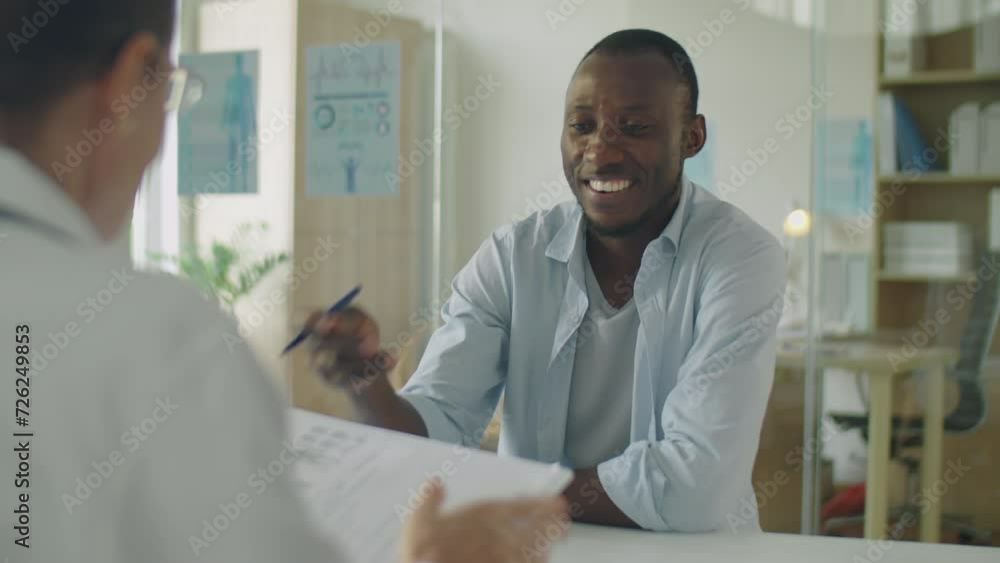 Young African American man walking in clinic, smiling and giving medical history to doctor while getting health consultation Young African American man walking in clinic, smiling and giving medical history to doctor while getting health consultation