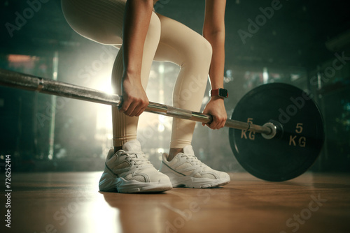 Young woman doing deadlift with heavy bar in gym, strong female athlete with muscular body lifting weights, exercising with barbell. photo