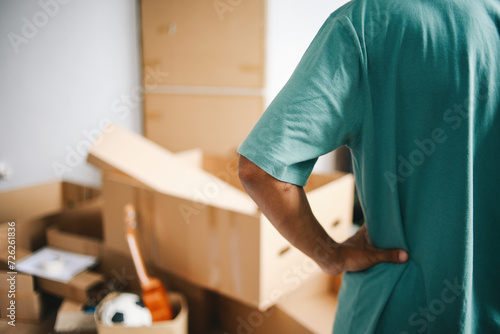Rear view of man standing and looking at pile of cardboard boxes in front of him. Relocation and moving house concept photo