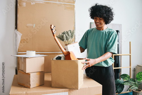 Young Asian man putting stuff into carton box preparing moving to new house