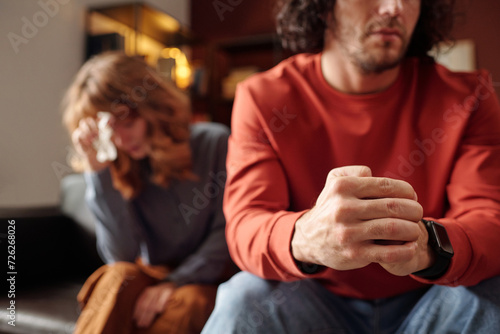 Selective focus shot of married couple experiencing relationship problems sitting on couch, woman crying and man avoiding her eyes