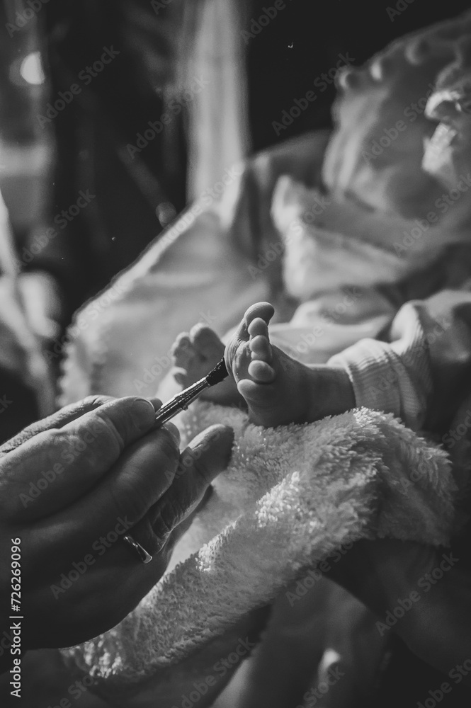 Baby leg. Unction at baptism. Closeup of tiny baby feet, the sacrament of baptism ceremony. Priest and godfather stretch hands to child legs. Temple, Orthodoxy. Anointing. Black and white photo