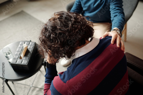 High angle view of unrecognizable psychologist comforting depressed man with messy curly hair giving him supportive touch