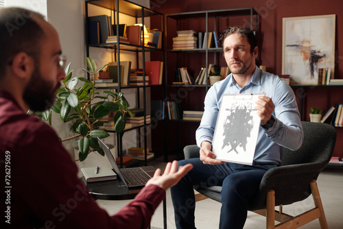 Professional psychologist examining patient demonstrating abstract picture to him photo