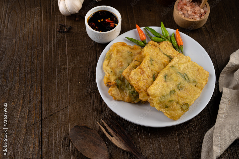 Deep fried tempeh or Tempe mendoan goreng made from soy bean with flour batter and spring onion on white plate. street food