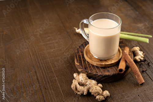 Hot ginger or wedang susu jahe milk with brown sugar, cinnamon, lemongrass and spice clove on wooden table.