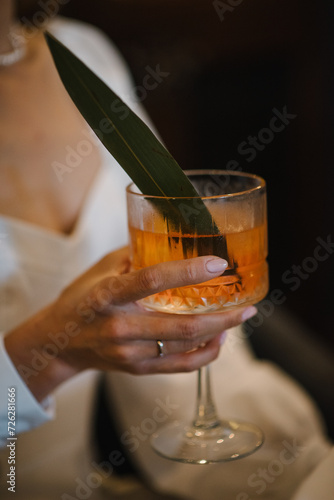 Woman drinking cocktail with slice of orange in a restaurant. Girl holding fresh juice. Female hand hold cocktail in glass on bar counter at nightclub. Closeup.