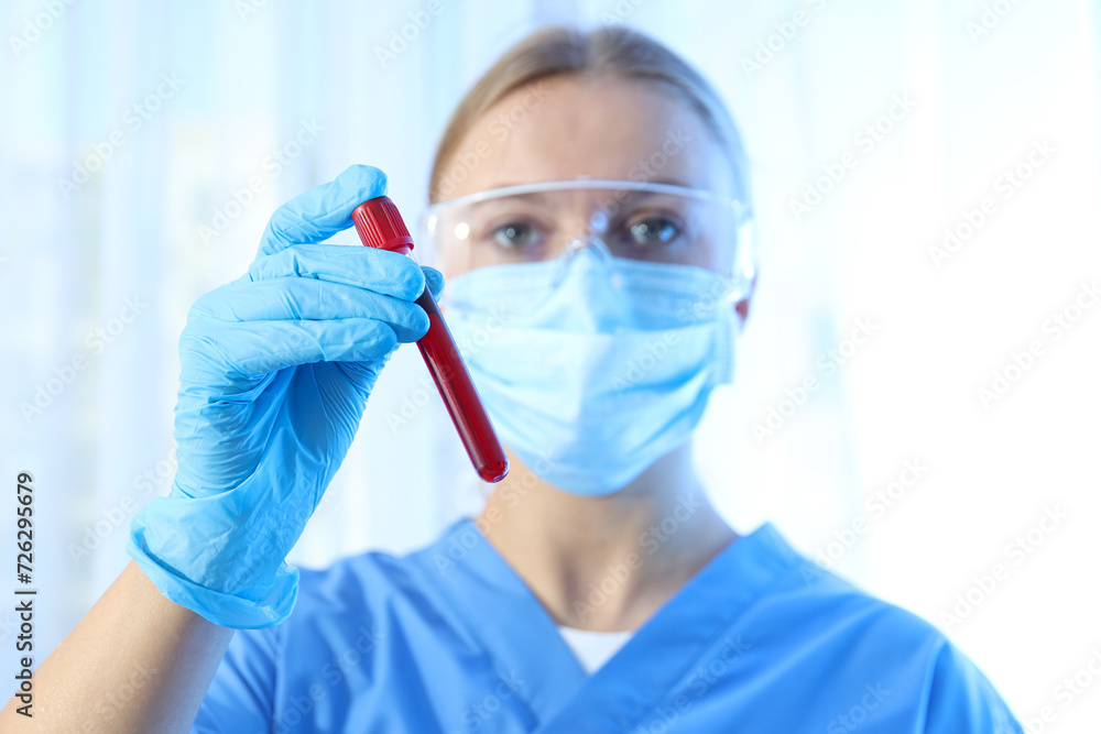 Laboratory assistant with test tube with donor blood in hand on blue background Laboratory assistant with test tube with donor blood in hand on blue background