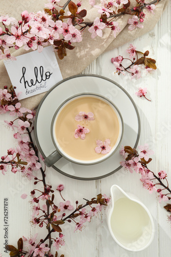 Spring twigs with flowers with a cup of hot drink, on a light wooden background.