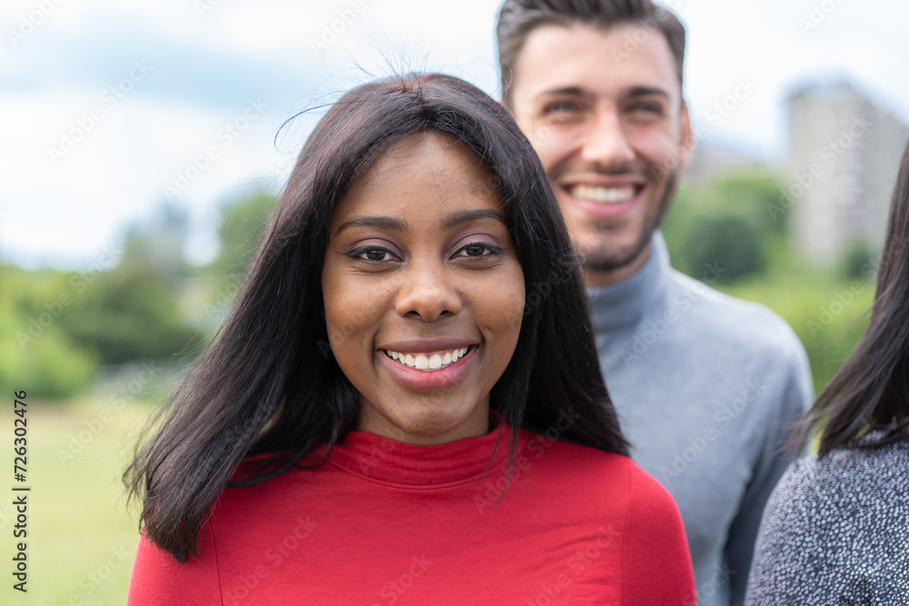Fototapeta premium Vibrant portrait of a smiling young woman with diverse friends in a park, showcasing joy and multicultural relationships.