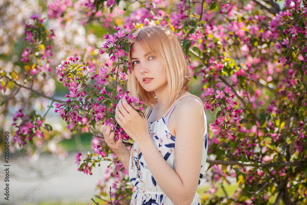 Portrait of an attractive young woman dressed in a dress posing against a background of blooming pink apple flowers. Portrait of an attractive young woman dressed in a dress posing against a background of blooming pink apple flowers.