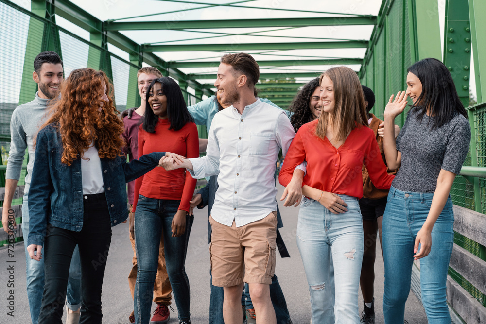 Obraz premium A group of multicultural friends walk relaxed and smiling on a city bridge, enjoying a day together.