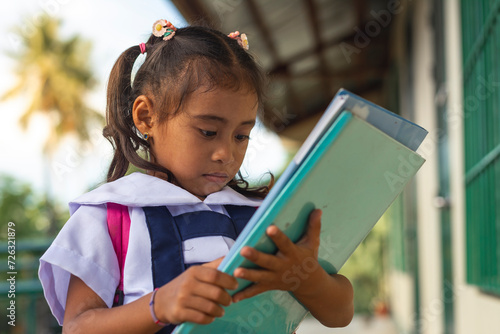 An attentive young student engrossed in reading a book, wearing a school uniform with a backpack. Outside a rural preschool. photo