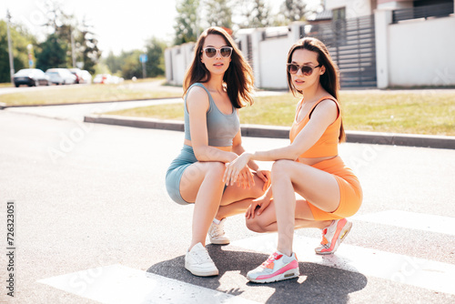 Two young beautiful smiling female in trendy summer cycling shorts, top clothes. Sexy carefree women posing in street at sunny day. Positive models having fun. Cheerful and happy