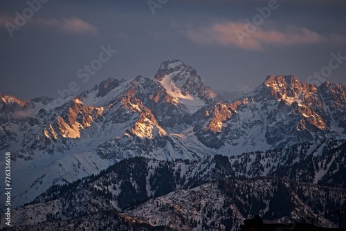 Beautiful view to the snowy winter mountain tops cloudy sky and golden hour sunlight