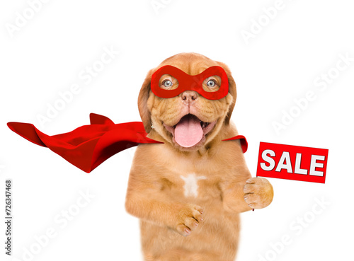 Funny Mastiff puppy with open mouth wearing superhero costume looking at camera and  showing signboard with labeled "sale". Isolated on white background