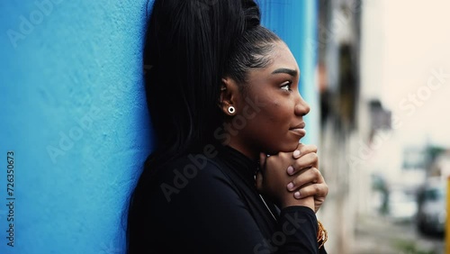 One hopeful young black woman gazing upwards with FAITH and GRATITUDE standing outside in city street. African American adult girl looking UP smiling in urban environment photo