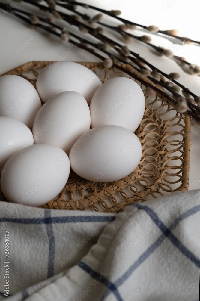 white chicken eggs lie on a brown wicker stand next to a willow branch, top view white chicken eggs lie on a brown wicker stand next to a willow branch, top view